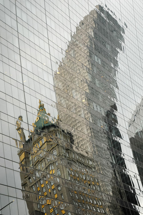 Stekleno pročelje zgradbe, ki odseva popačeno sliko dveh sosednjih stavb.