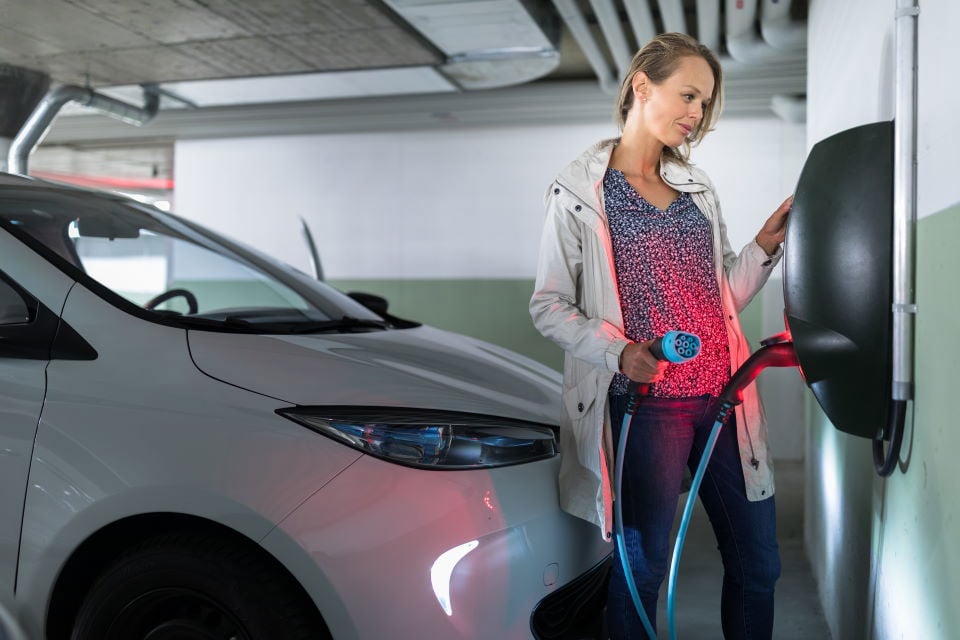 Femeie care se pregătește să conecteze mașina ei electrică la un încărcător de perete într-un garaj subteran.