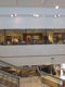 Pogled na bel razstavni prostor in požarno odporno steklo brez okvirjev Promat®-SYSTEMGLAS F1 60. Steklena okna so po celotnem obsegu prostora v Pohištvenem centru Lesnina v Kopru, v levem delu slike so stopnice, ki vodijo navzdol. 