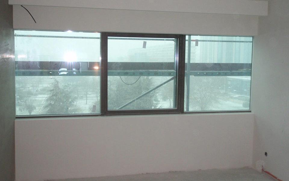 Na sliki je nedokončan notranji prostor s tremi kvadratnimi okni in pogledom ven na stavbe v okolici v Crowne Plaza hotel Beograd. 