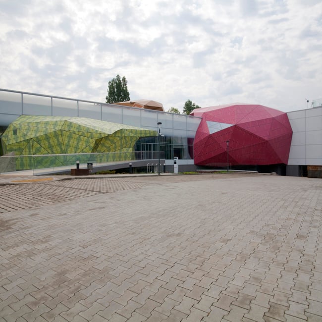 Na slici je Muzeiko dječji muzej. Središnji dio muzeja je crvene boje dok lijevom i desnom stranom prevladava staklo. Put do muzeja je napravljen od tlakovca.