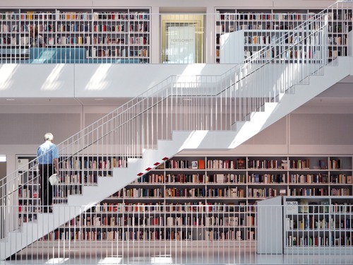 Pogled na dva nivoa moderno dizajnirane biblioteke koji su povezani dijagonalnim stepeništem i čije su police pune knjiga.