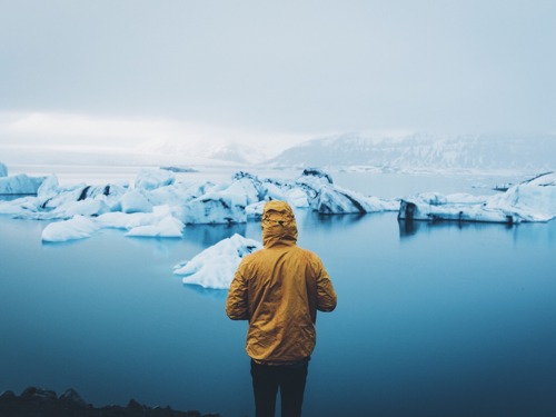 Na slici je osoba u žutoj jakni sa kapuljačom koja gleda u ledenjake na moru.