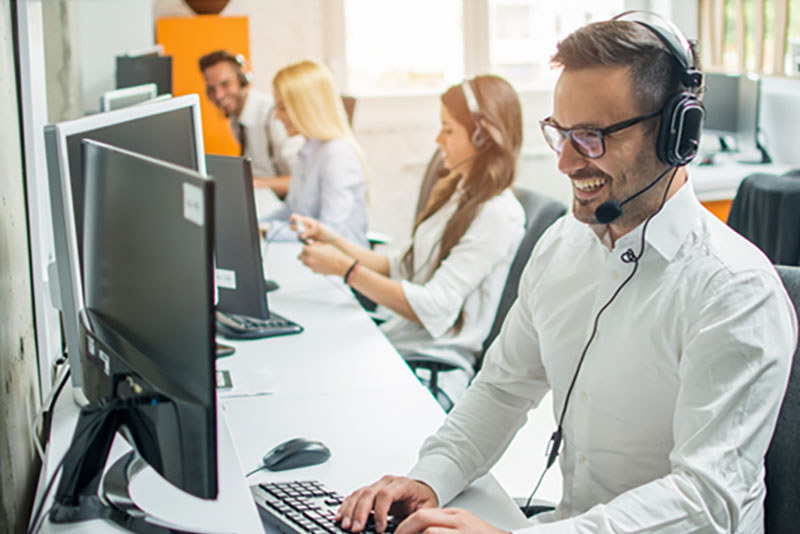 Muži a ženy sedia pri počítačoch v call centre so sluchátkami a mikrofónmi.