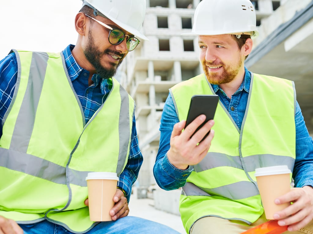 Dvaja projektanti na stavenisku, ktorí sa pozerajú na mobilný telefón.